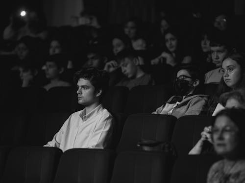 Grayscale Photo of a Man Sitting in the Audience