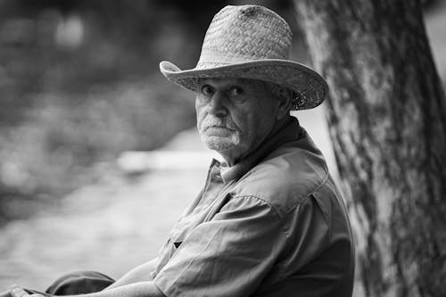 Grayscale Photo of an Elderly Man Wearing a Woven Hat