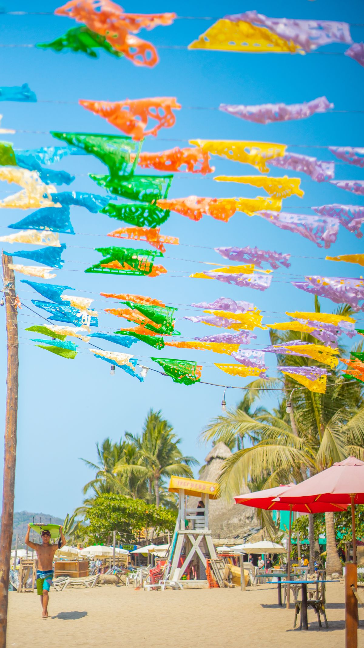 Colorful flags flutter above a lively beach scene in Sayulita, Mexico, capturing the essence of summer.