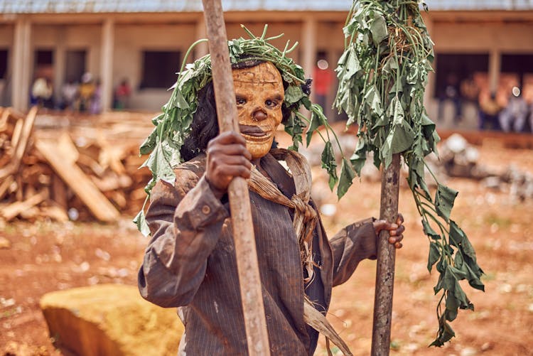 Person Wearing A Mask Holding Wooden Sticks With Wilted Leaves