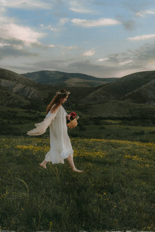 Woman With Basket Full of Flowers Walking on Meadow Near Mountains