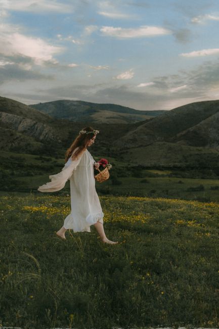 A serene image of a woman in a flowing dress walking barefoot through a meadow, carrying a basket of flowers.