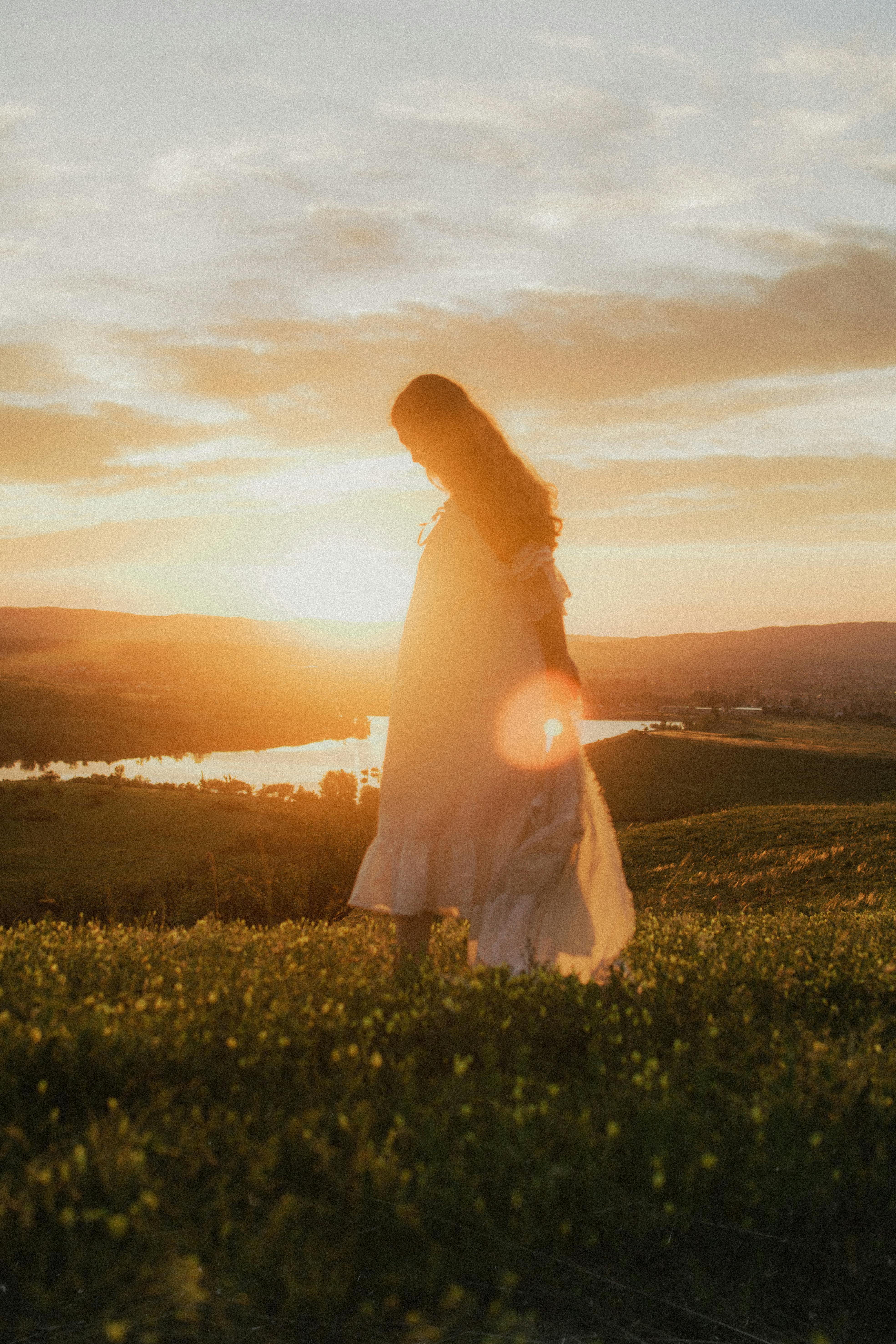Woman in a white dress walking through a sunlit field at sunset, capturing a serene moment in nature.