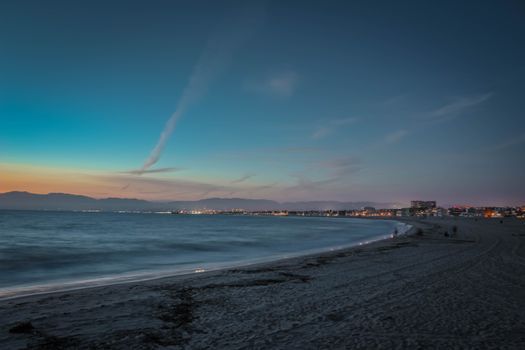 Captivating beach scene at twilight with distant city lights and tranquil ocean waves.