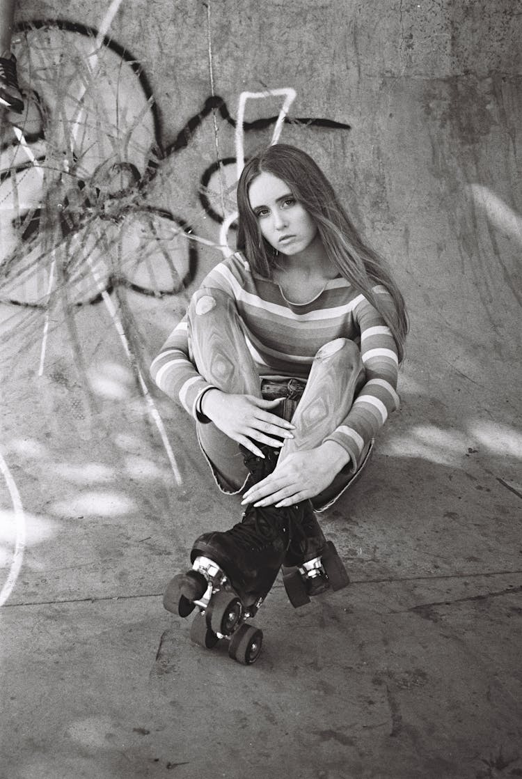 Woman In Rollerskates Sitting Cross Legged On Concrete In A Skatepark