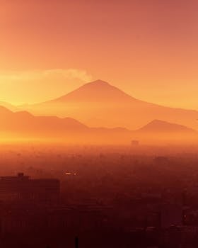 A mesmerizing view of a mountain shrouded in fog, captured at sunrise with warm orange hues.