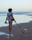 Woman in White and Black Floral Shirt and Blue Denim Shorts Standing on Beach Shore With Beside