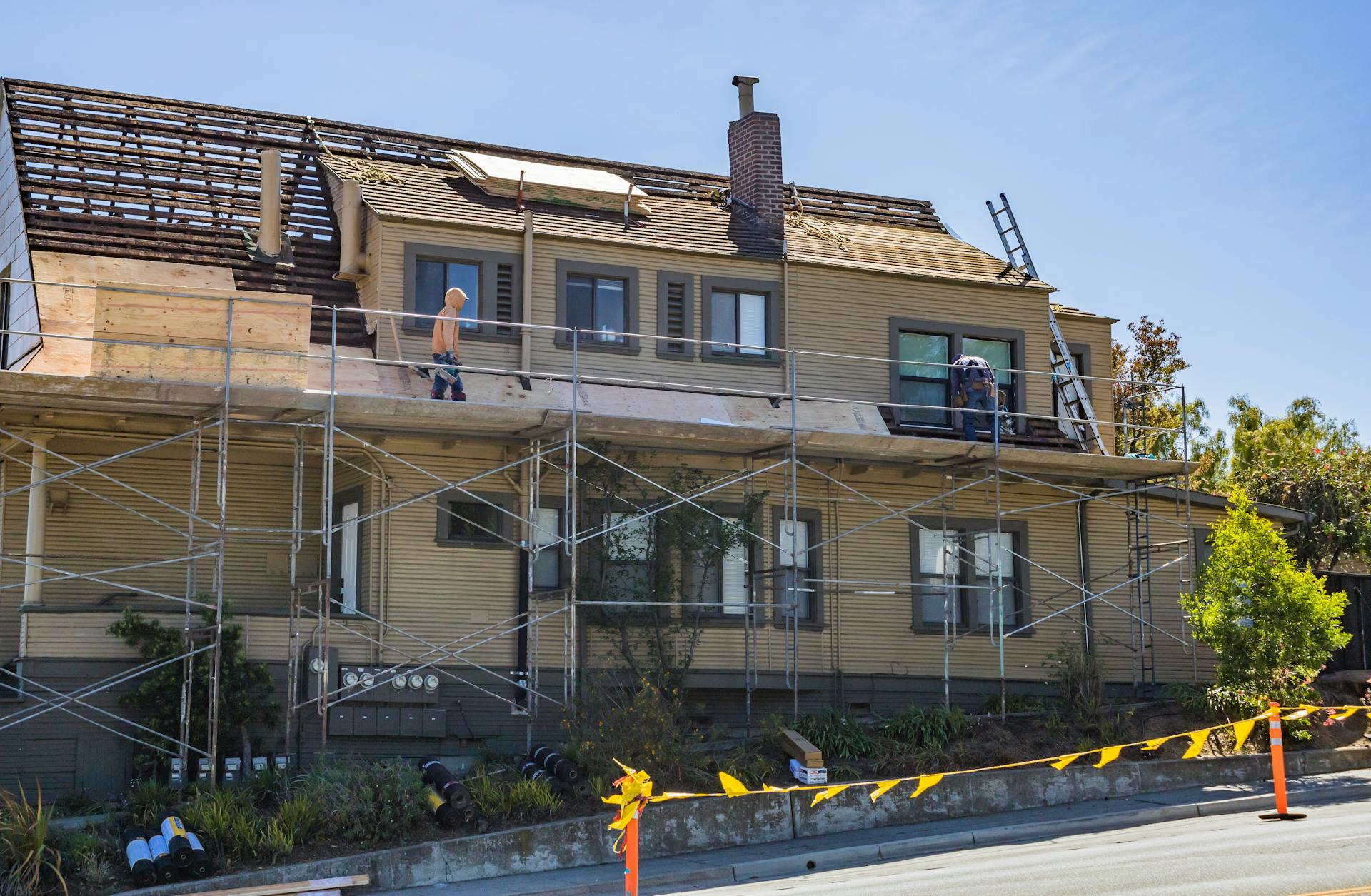 House under renovation with scaffolding and workers fixing the roof on a sunny day.