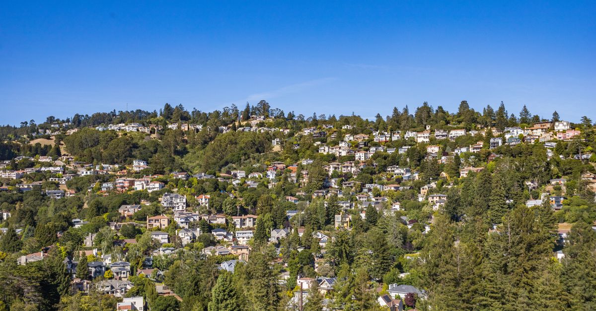 A scenic aerial view of a lush residential area on a hillside under clear blue skies.