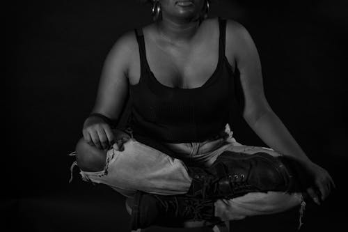 A Grayscale of a Woman in a Tank Top and Denim Pants Sitting on a Chair