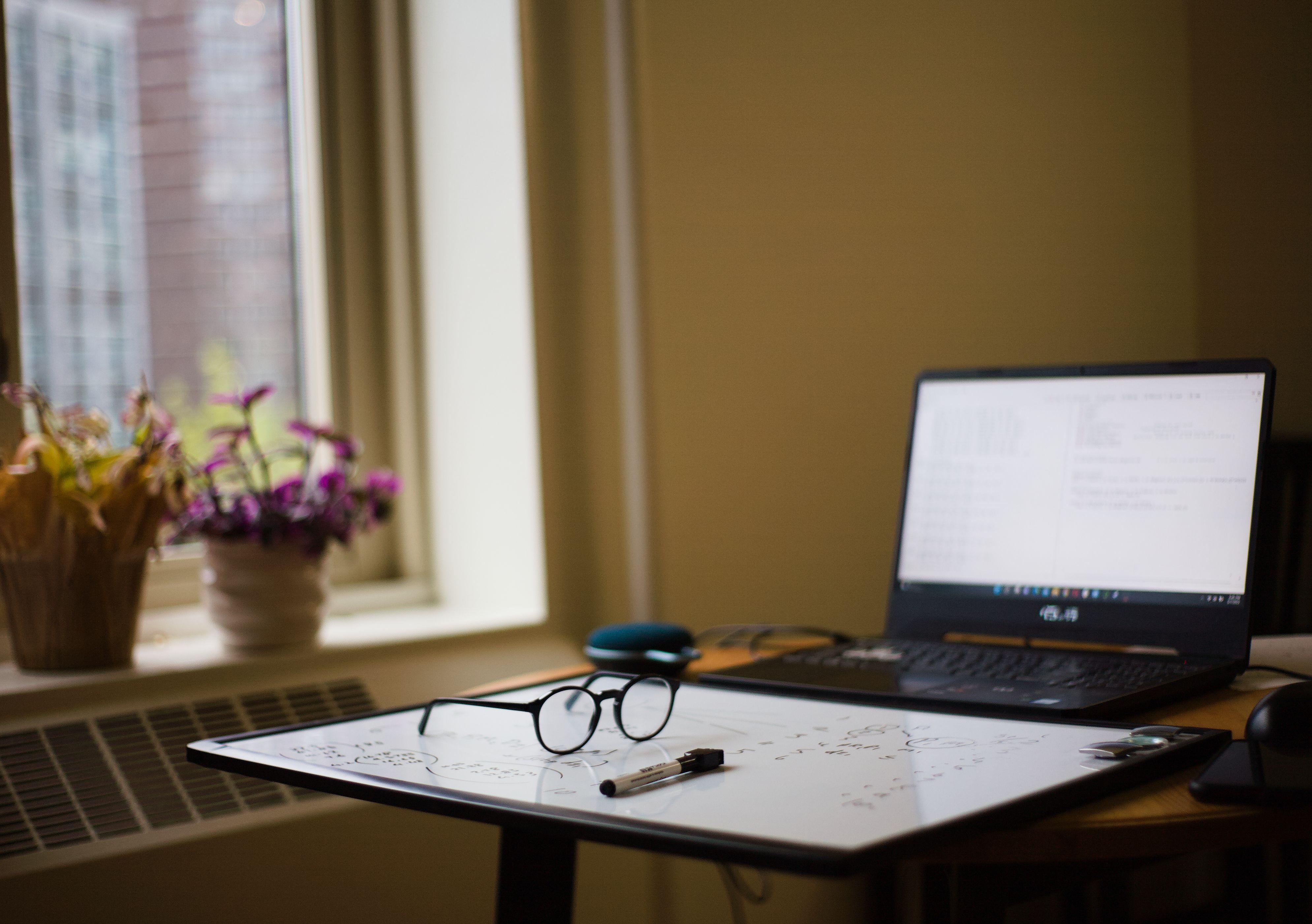 a cozy home office with a plant, a laptop, and a small whiteboard with goals