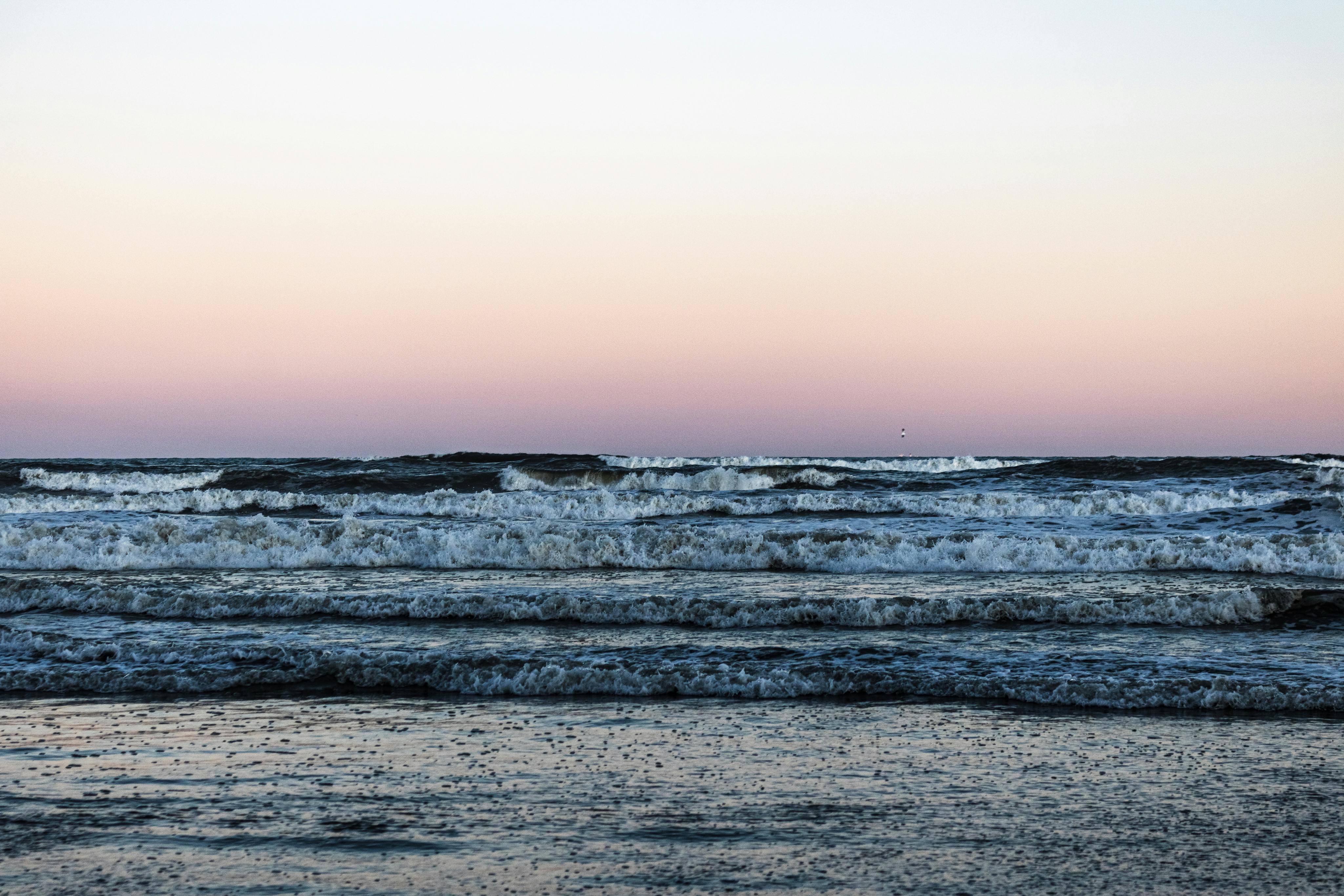 Vista serena de las olas del océano bajo un cielo pastel al atardecer, reflejando tranquilidad.