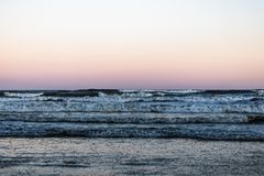 Rustig uitzicht op oceangolven onder een pastelhemel bij schemering, die rust weerspiegelt.