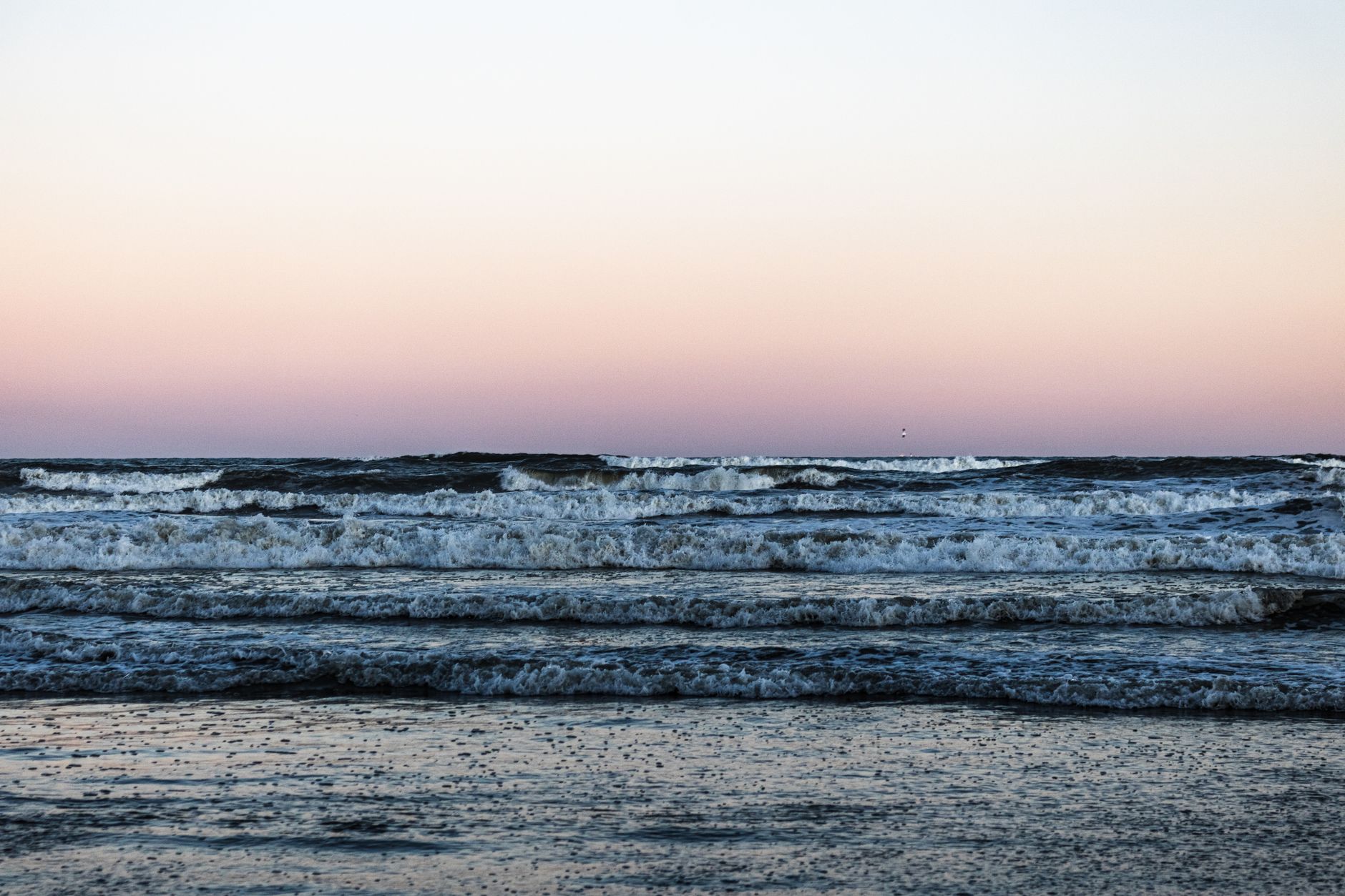 Vista serena de las olas del océano bajo un cielo pastel al atardecer, reflejando tranquilidad.