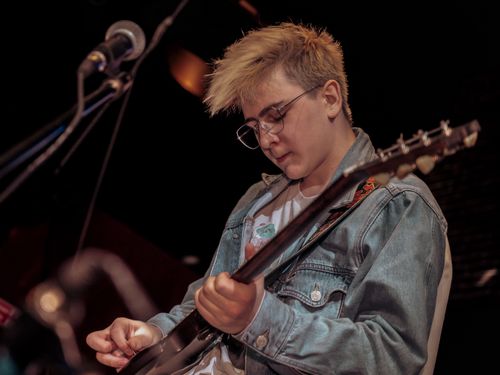 Free Teen guitarist wearing denim jacket performs passionately at a live music show. Stock Photo