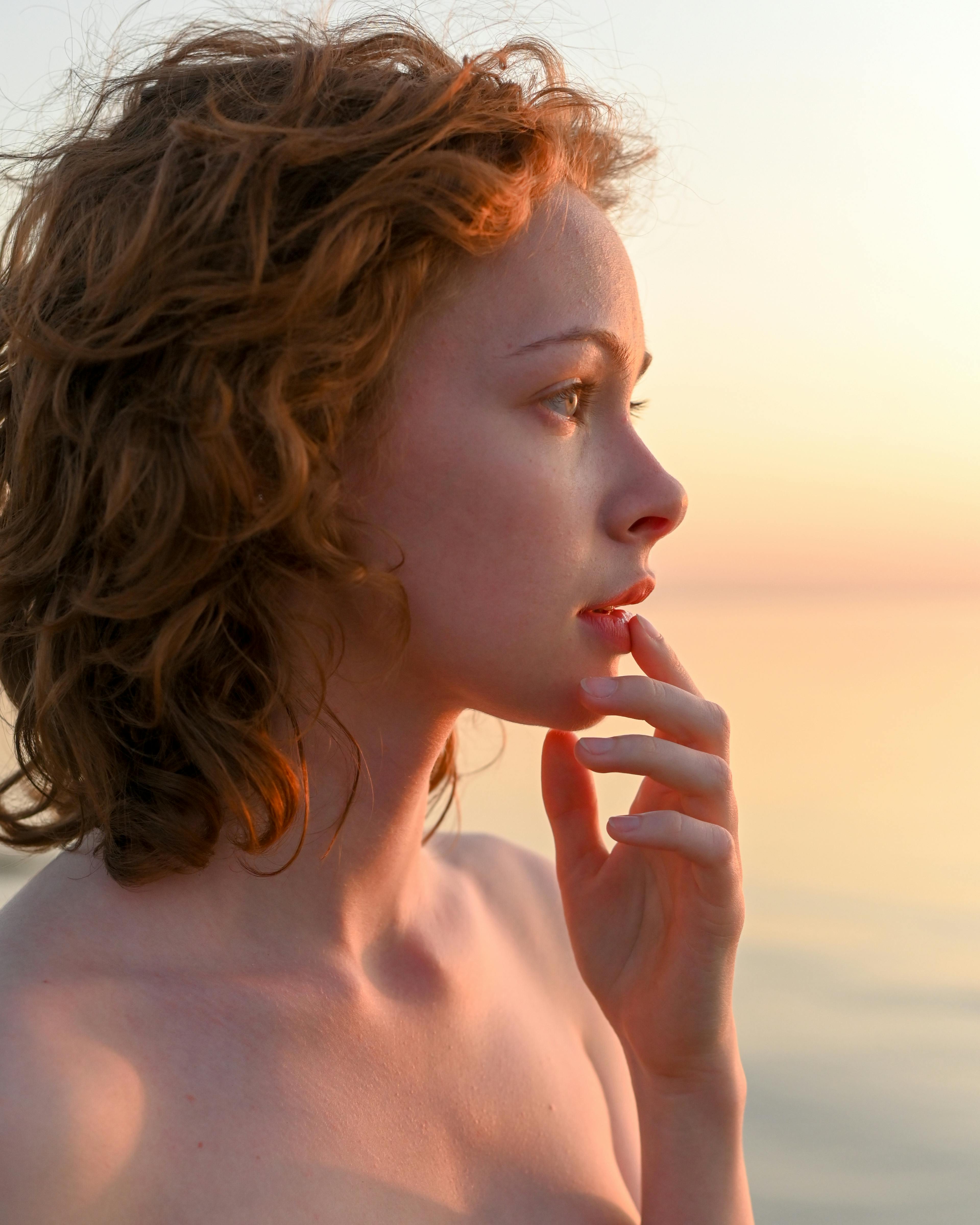 undressed redhead woman with hand on chin in sunset light