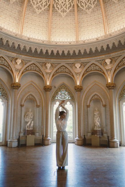 A graceful woman poses with hands above head inside the ornate Monserrate Palace, Sintra.