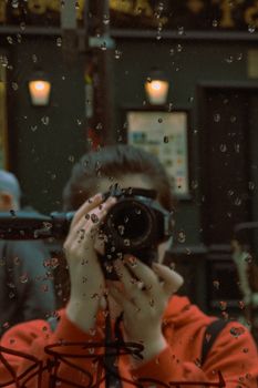 A person with a camera photographing through a rain-speckled window in Paris.