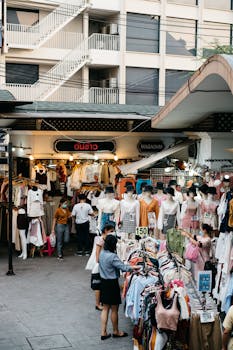 Crowded street market with various clothes on display and people shopping.