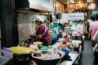 Street food vendor in a bustling Bangkok market kitchen preparing dishes with fresh ingredients.