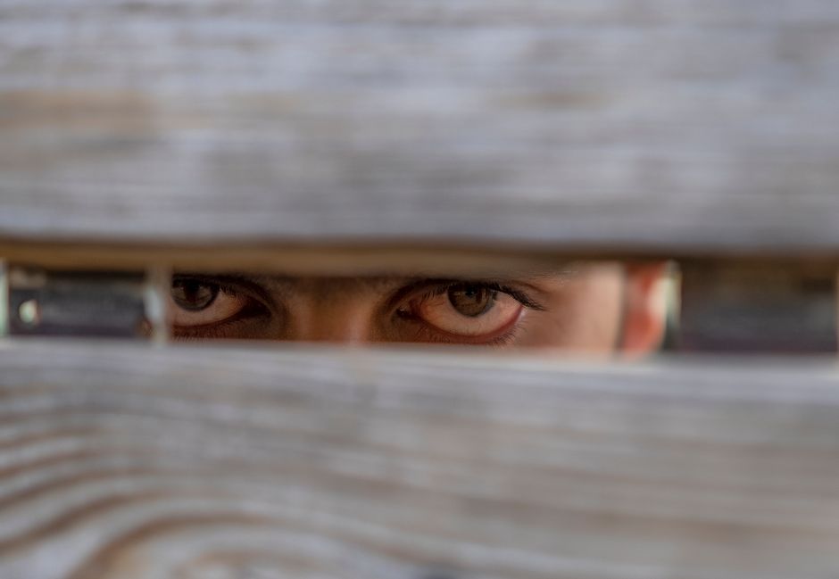 Mysterious eyes peering through a wooden fence. Concept of curiosity and hidden observation.
