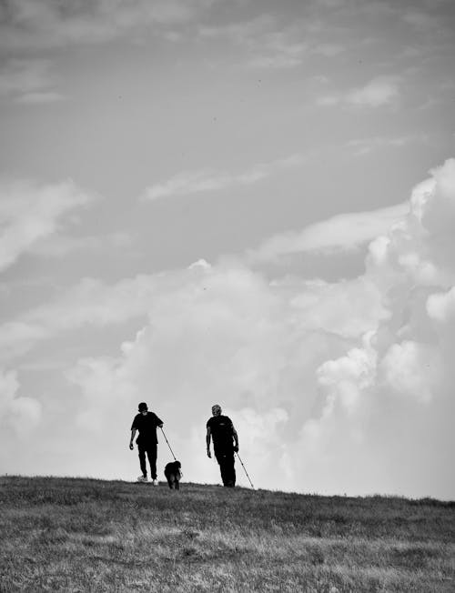 A Grayscale Photo of Men Walking on the Field with Their Dog