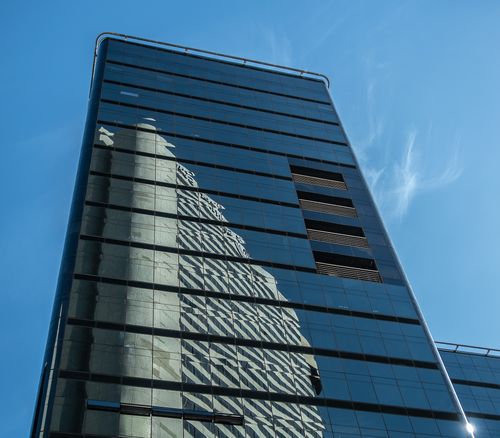 Free A modern high-rise building with mirrored facade reflecting another skyscraper under a clear blue sky in Cape Town. Stock Photo