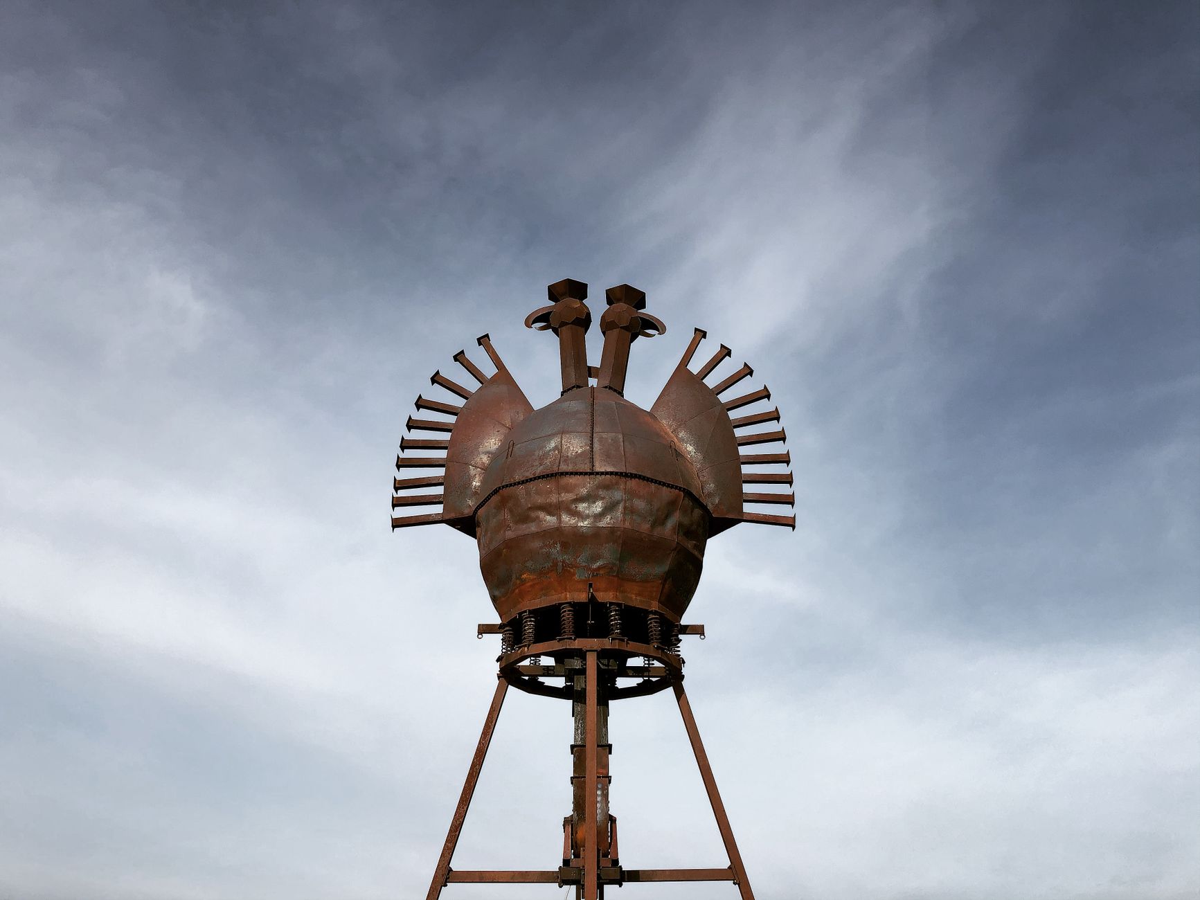 A striking metal sculpture towers against a backdrop of a cloudy sky, showcasing artistic industrial design.