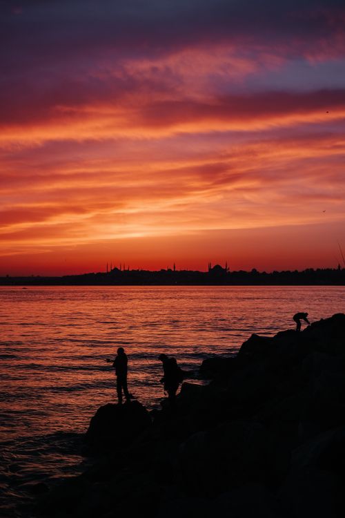Free People silhouetted by a vibrant red sunset over the sea, offering a dramatic and serene scene. Stock Photo