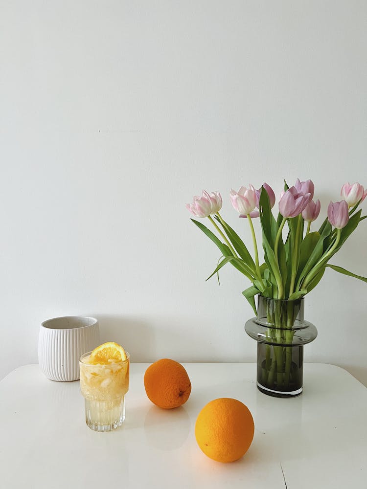 Orange Fruits Beside A Bouquet Of Tulip Flowers In Vase And A Glass Of Water