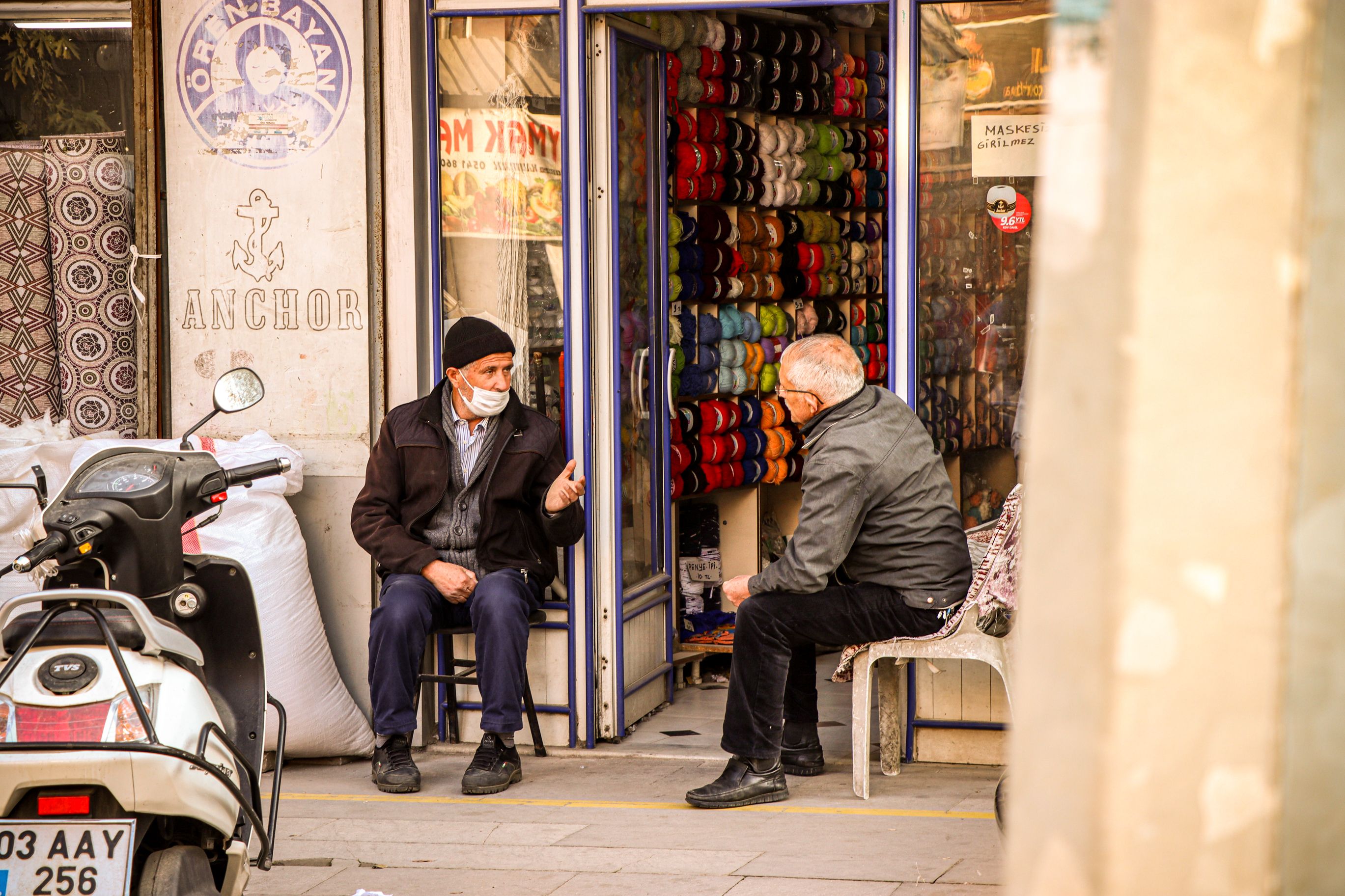 Two elderly men in Afyonkarahisar, Turkey, engage in conversation outside a yarn shop.