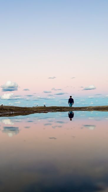 A man walks along Clovelly Beach at dawn with serene reflections and pastel skies.