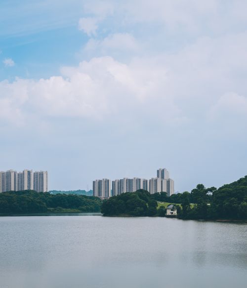 Free High-rise buildings with a serene lake and lush greenery under a blue sky. Stock Photo