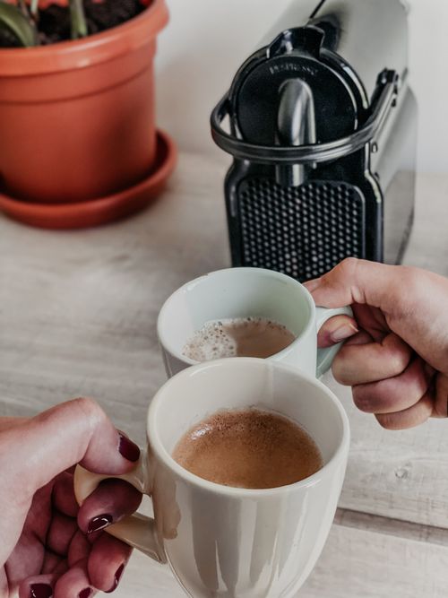 Free Two people holding cups of coffee by an espresso machine with a plant pot in the background, indoors. Stock Photo
