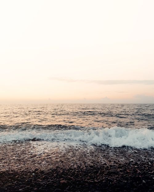 Free Peaceful ocean waves gently rolling onto a rocky beach during sunset, creating a tranquil seascape. Stock Photo