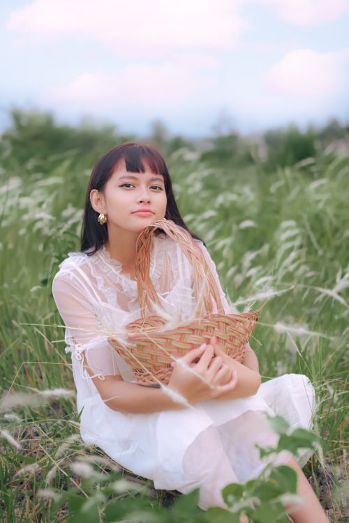 Free A woman sitting in a field holding a basket, showcasing a serene and natural vibe. Stock Photo