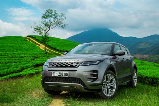 Range Rover SUV parked in lush green tea fields of Vietnam with scenic mountains.