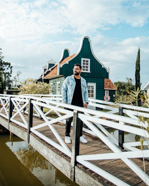 A Bearded Man in Denim Jacket Standing on a Wooden Bridge