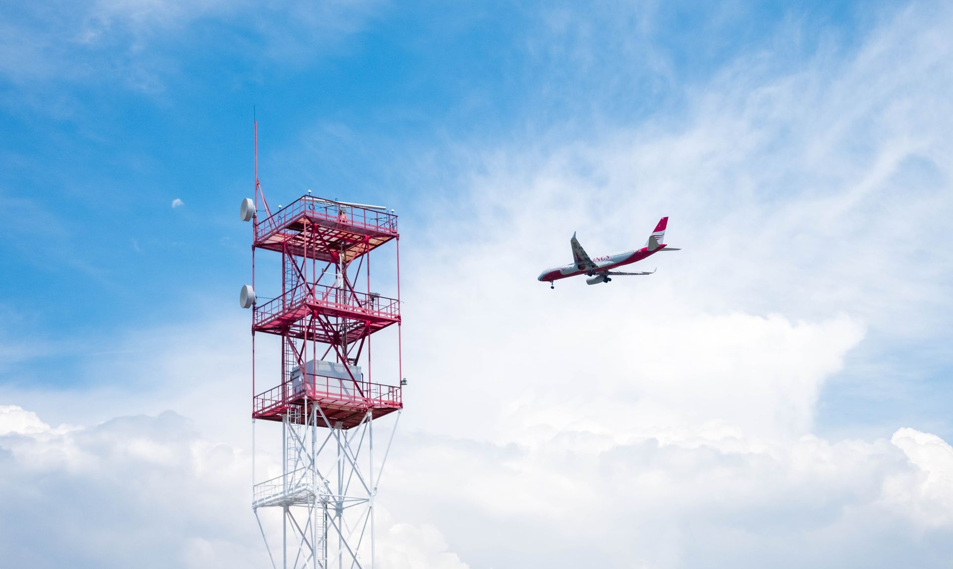 Airplane approaches communication tower against a bright blue sky in Sochi, Russia.