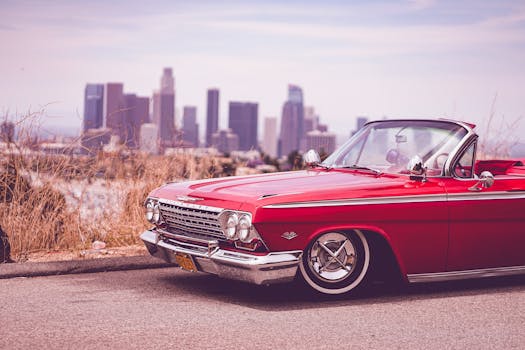 A vintage red Chevrolet Impala parked with Los Angeles skyline in the backdrop.