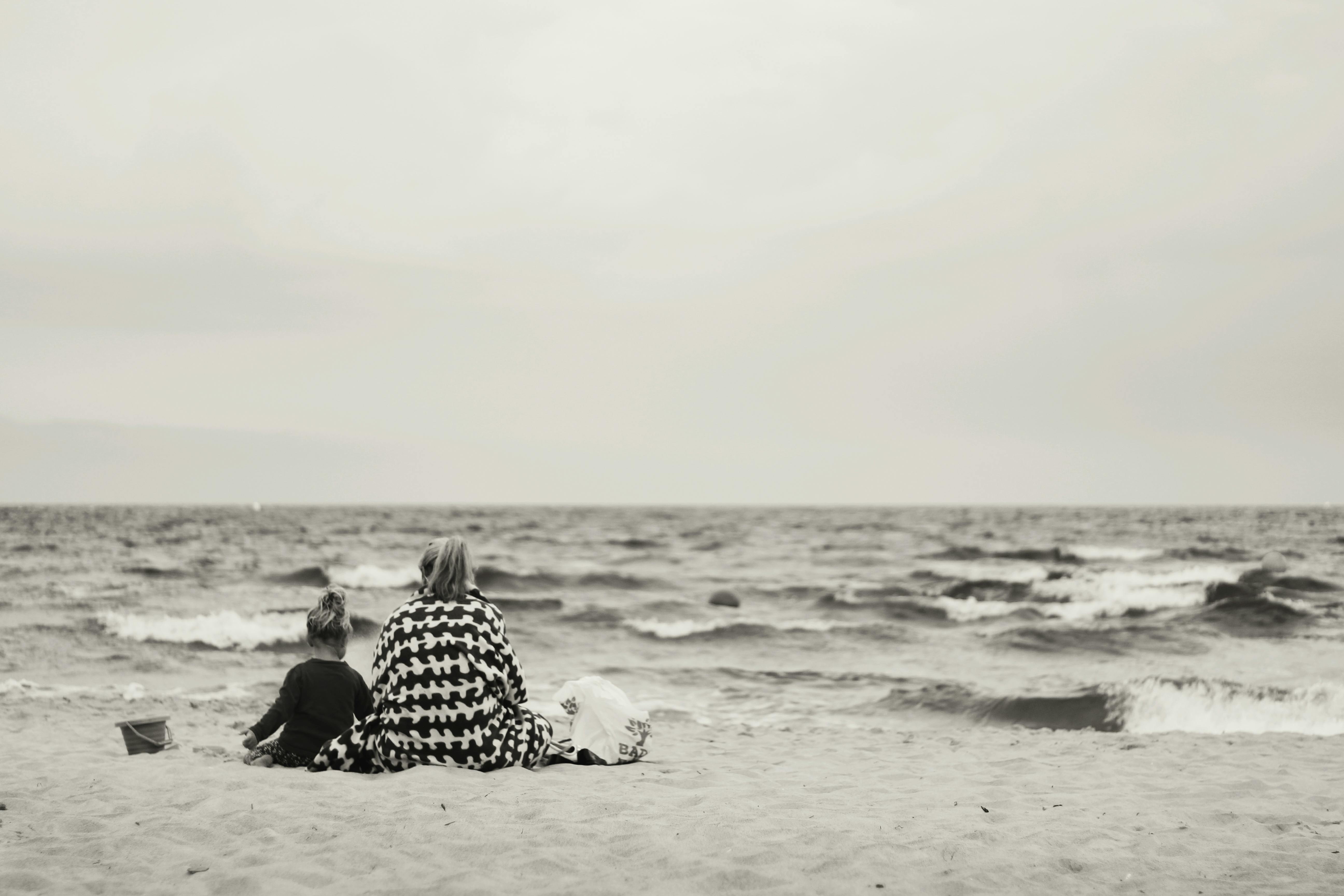 Gratuit Femme Et Enfant Assis Sur Le Sable Près Du Plan D'eau Photos