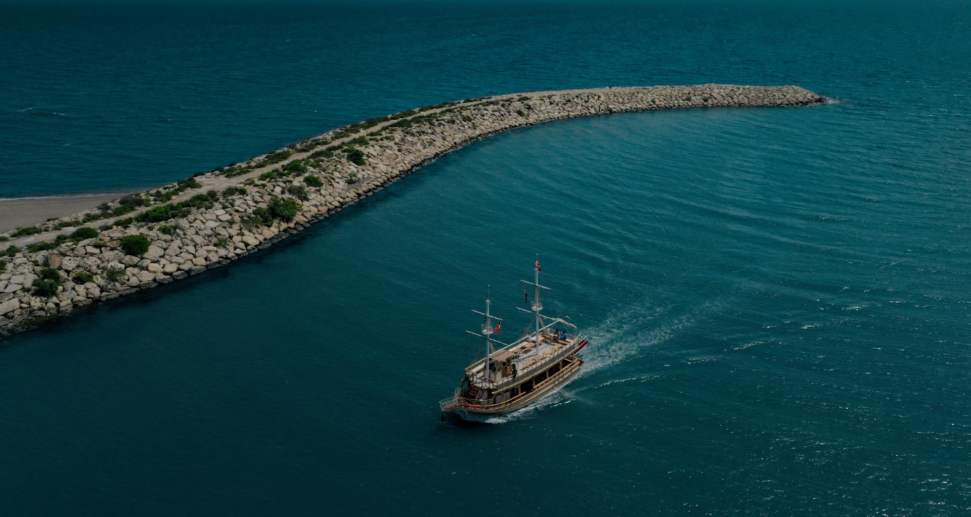 A sailing ship navigates the blue waters near a rock breakwater in Antalya, Turkey, capturing a serene aerial scene.