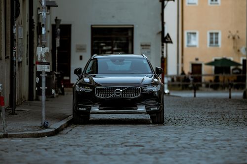 Free Elegant black Volvo car parked on a cobblestone street in a charming town setting. Stock Photo