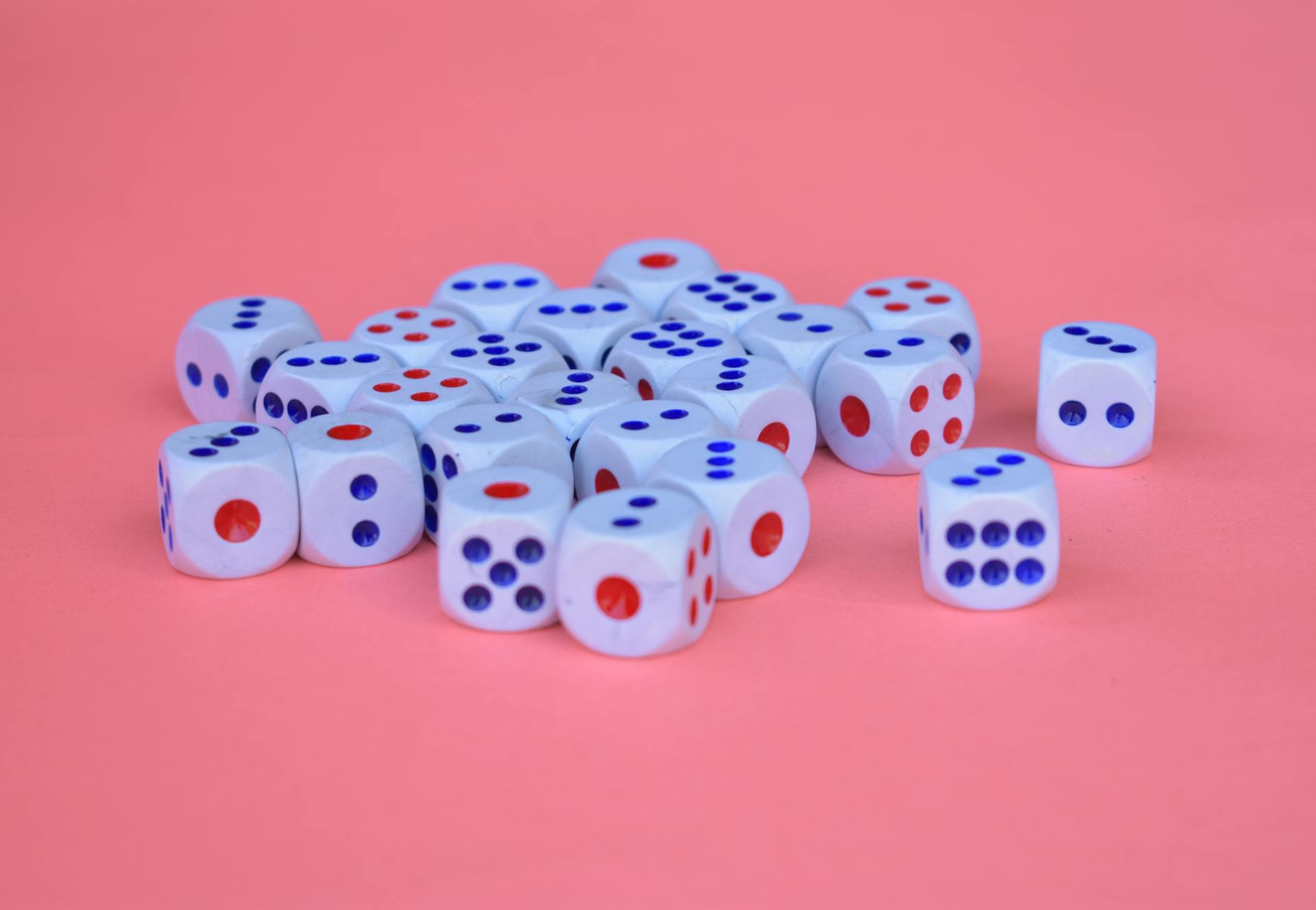 A collection of white dice with red and blue dots arranged on a pink surface.