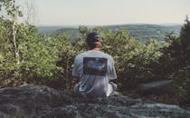 阳光明媚的日子里，一名男子坐在岩石上欣赏山景