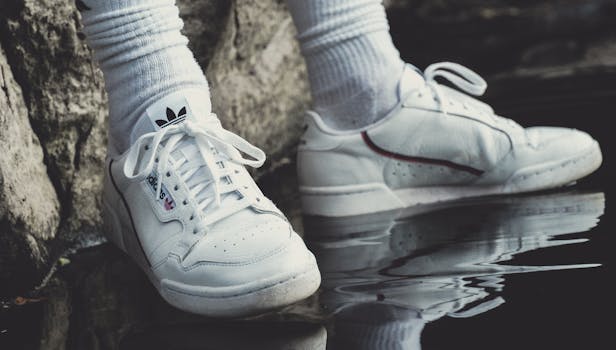 Close-up of white sneakers and socks reflecting on water next to a rock.