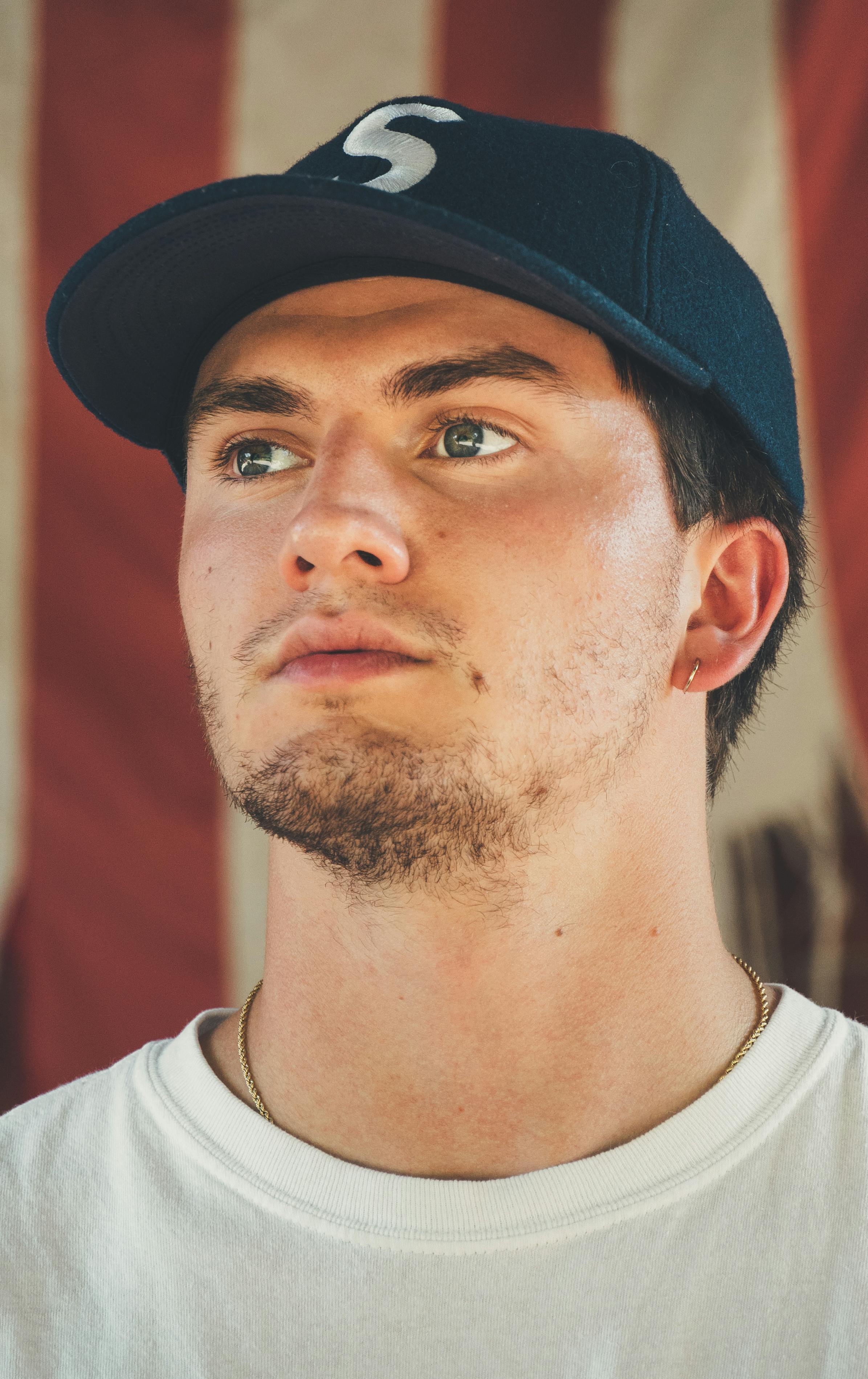 Portrait of a young man in a casual cap and t-shirt with a thoughtful expression.