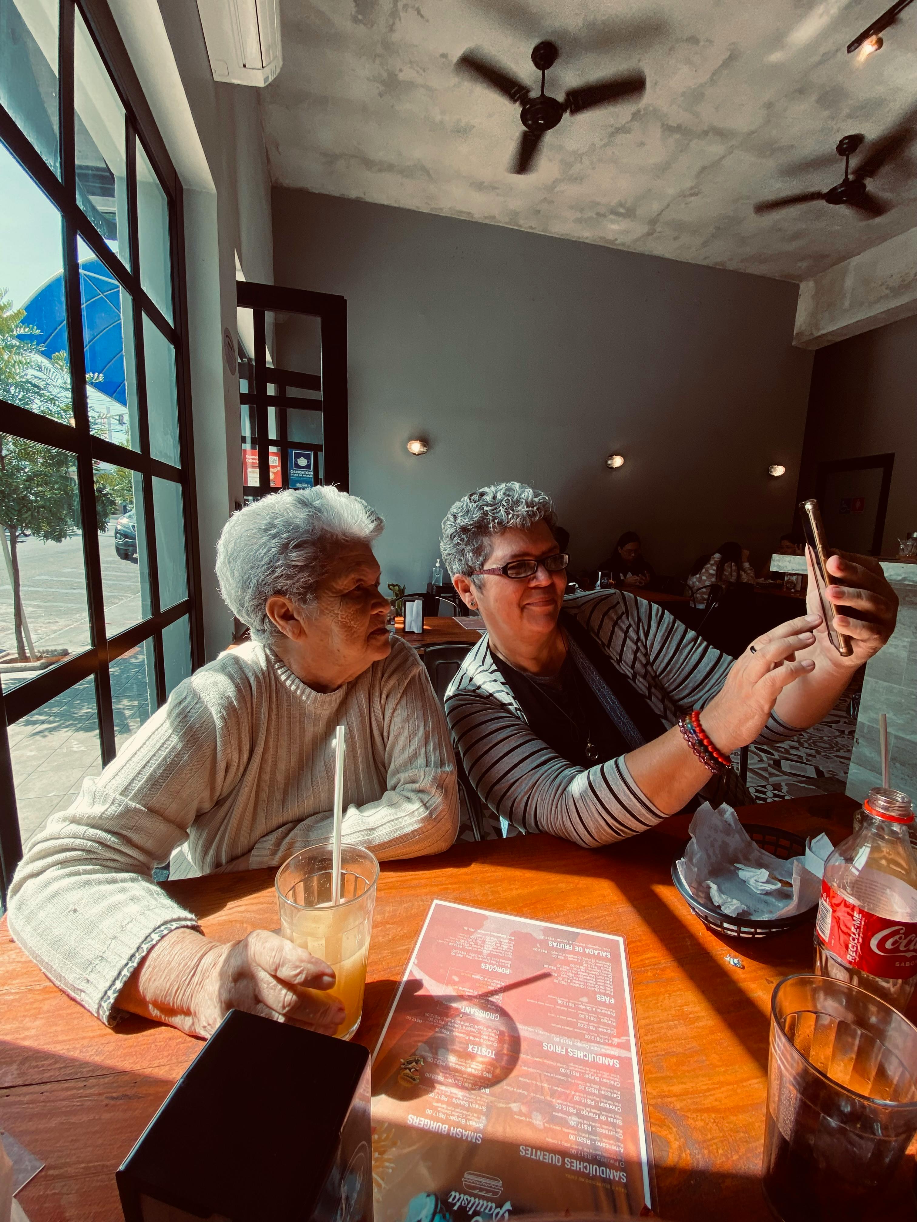 Free Two elderly women enjoying a selfie moment in a Brazilian café. Perfect for lifestyle imagery. Stock Photo