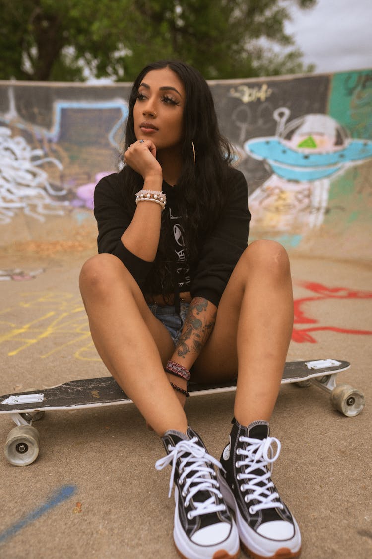 Young Woman Sitting On Skateboard In Skate Park