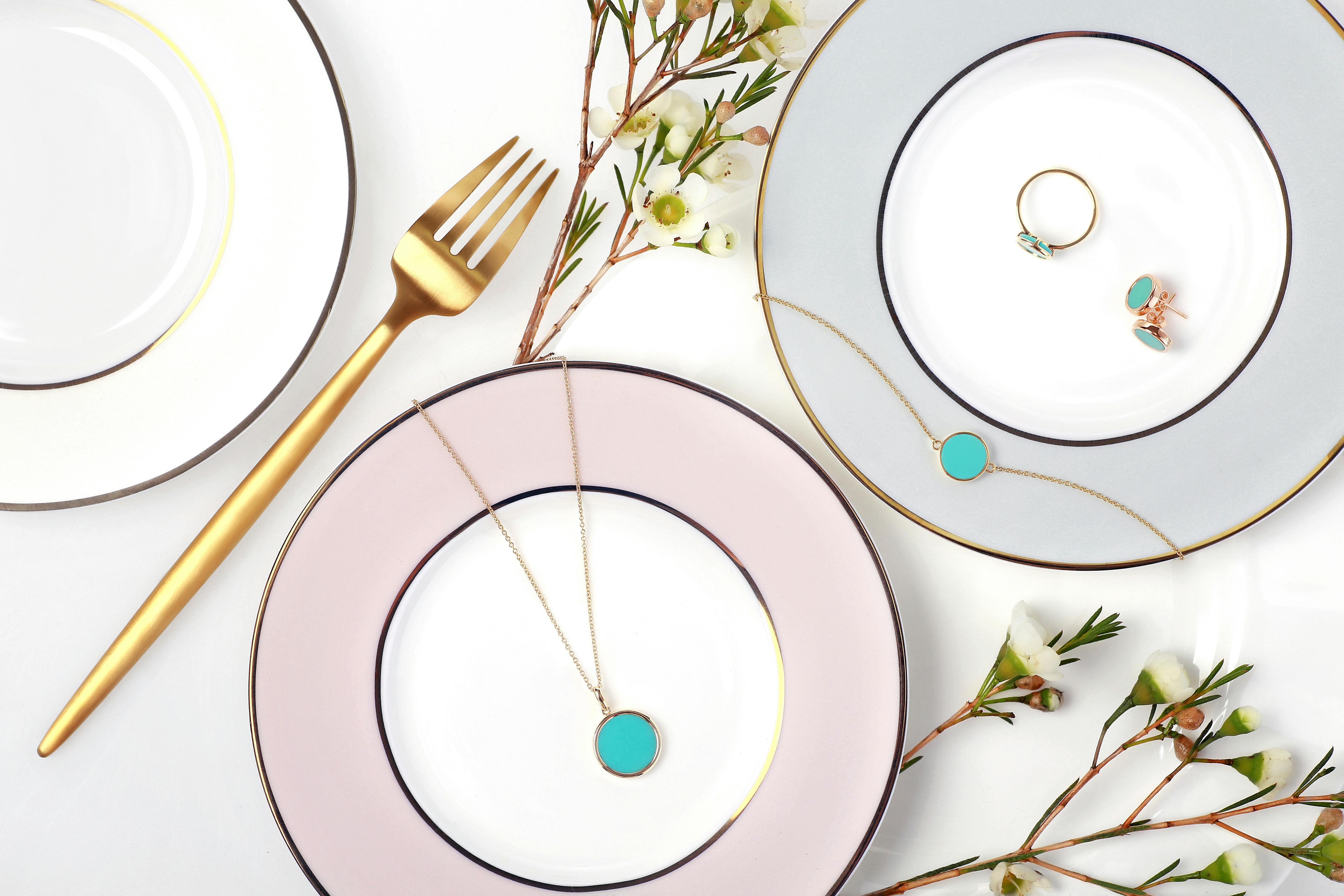 Several delicate 14K gold pendant necklaces arranged on a neutral surface, minimalist fine jewelry flat lay photography